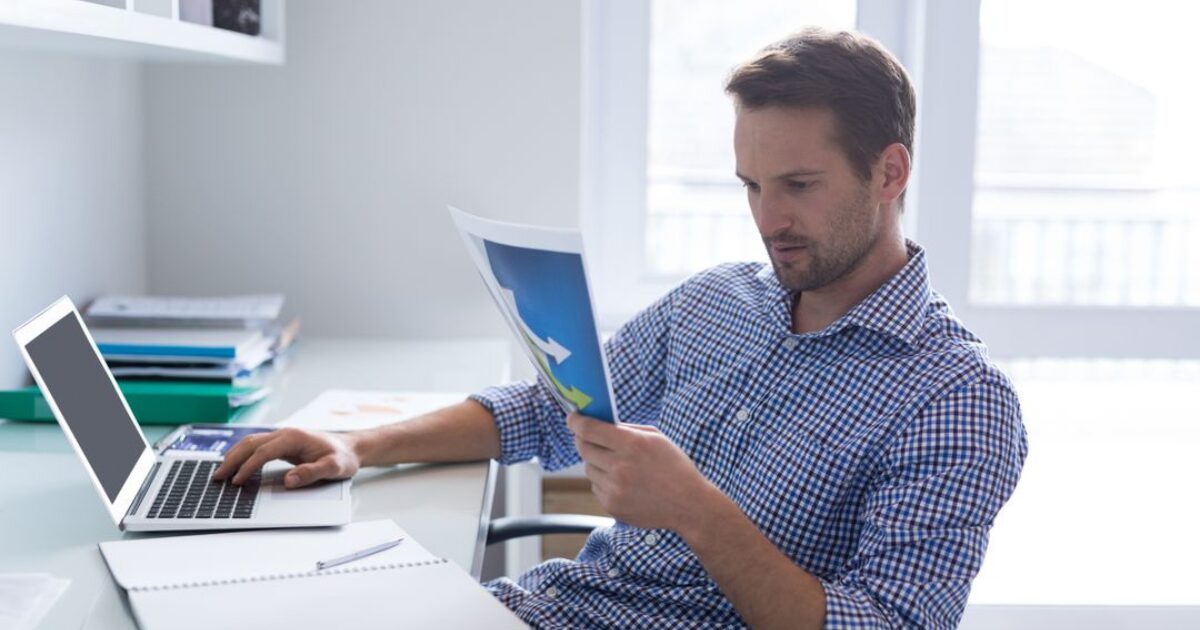 ノートパソコンと手書きメモ、グラフ資料が並ぶデスクで、ネットワーク構造を分析している作業環境が写っている写真