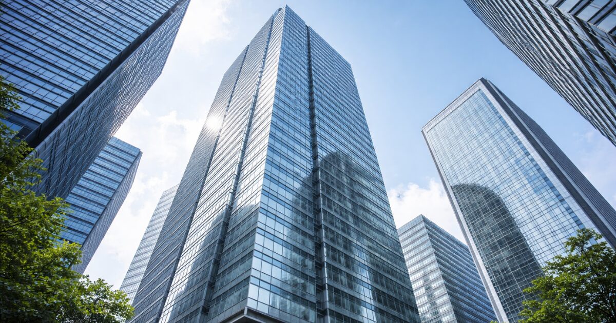 複数の高層オフィスビルが並び立つ都市風景を下から見上げた構図で、それぞれ異なる構造や配置の建物が並ぶ様子が、企業ごとのビジネスモデルの違いを理解するイメージとして写っている。